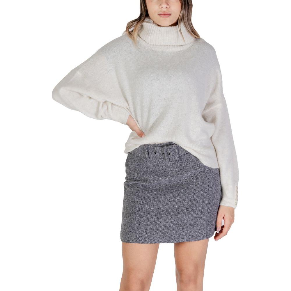 Woman wearing ICHI Cream Acrylic Sweater, fall/winter knitwear, paired with a gray skirt, showcasing cozy, stylish fashion.