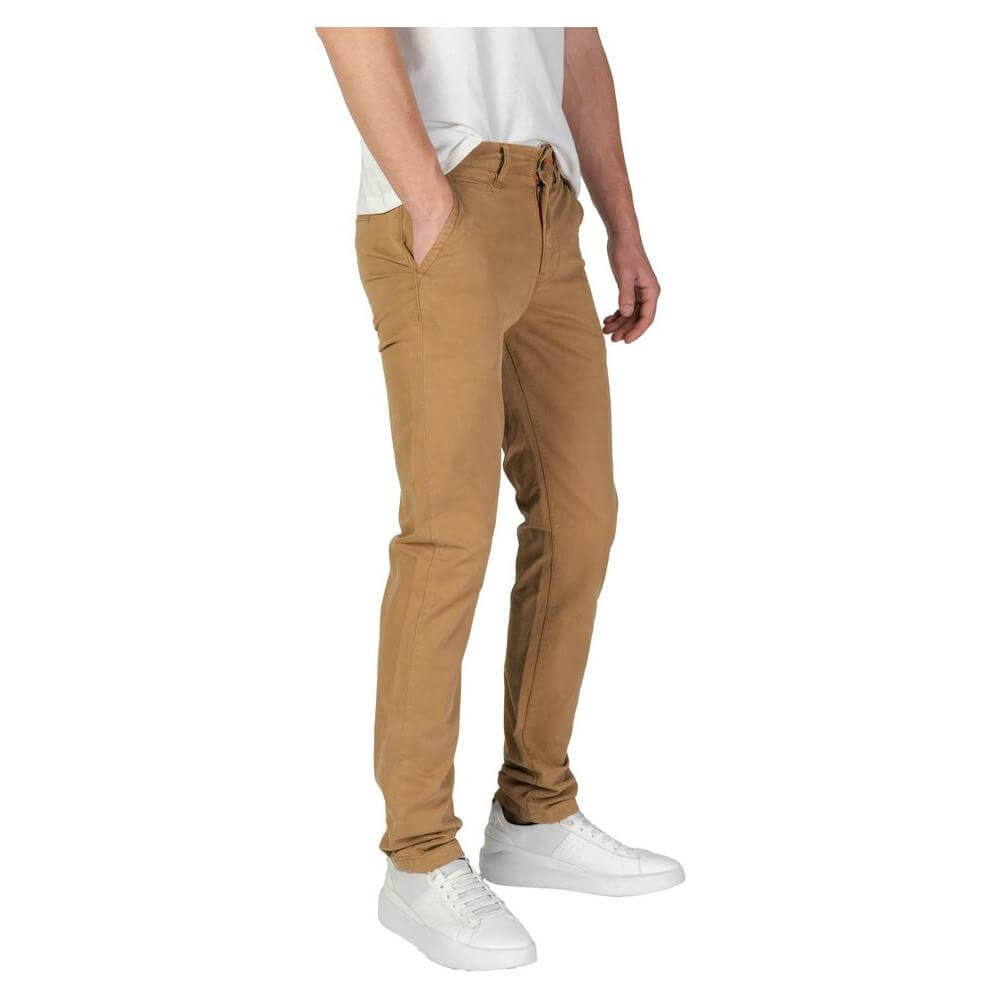 Man wearing Superdry beige cotton slim pants, fall winter collection, with white sneakers and casual white shirt.