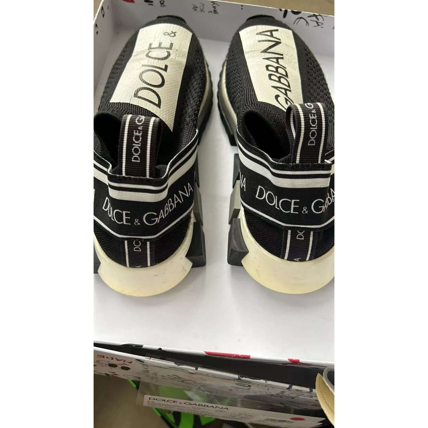 Dolce & Gabbana black and white Sorrento sneakers with logo print and black rubber sole, shown in box, back view.